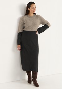 Stickad klänning med en beige topp och svart botten, med långa ärmar, rundad halsringning och en texturerad yta. Kombineras med knähöga bruna stövlar.