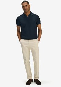 Navy short-sleeve polo shirt with a soft texture, featuring a wider collar, paired with beige trousers and dark brown loafers.