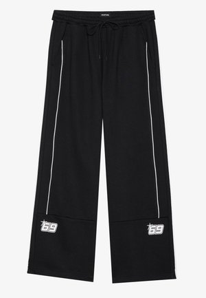 Fekete melegítőnadrág rugalmas derékkal és húzózsinórral, fehér oldalsávokkal és nyomott logóval a bal alsó lábon.