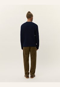 Navy knitted sweater with a textured pattern, crew neck, and ribbed cuffs, paired with olive corduroy pants and a brown beanie.