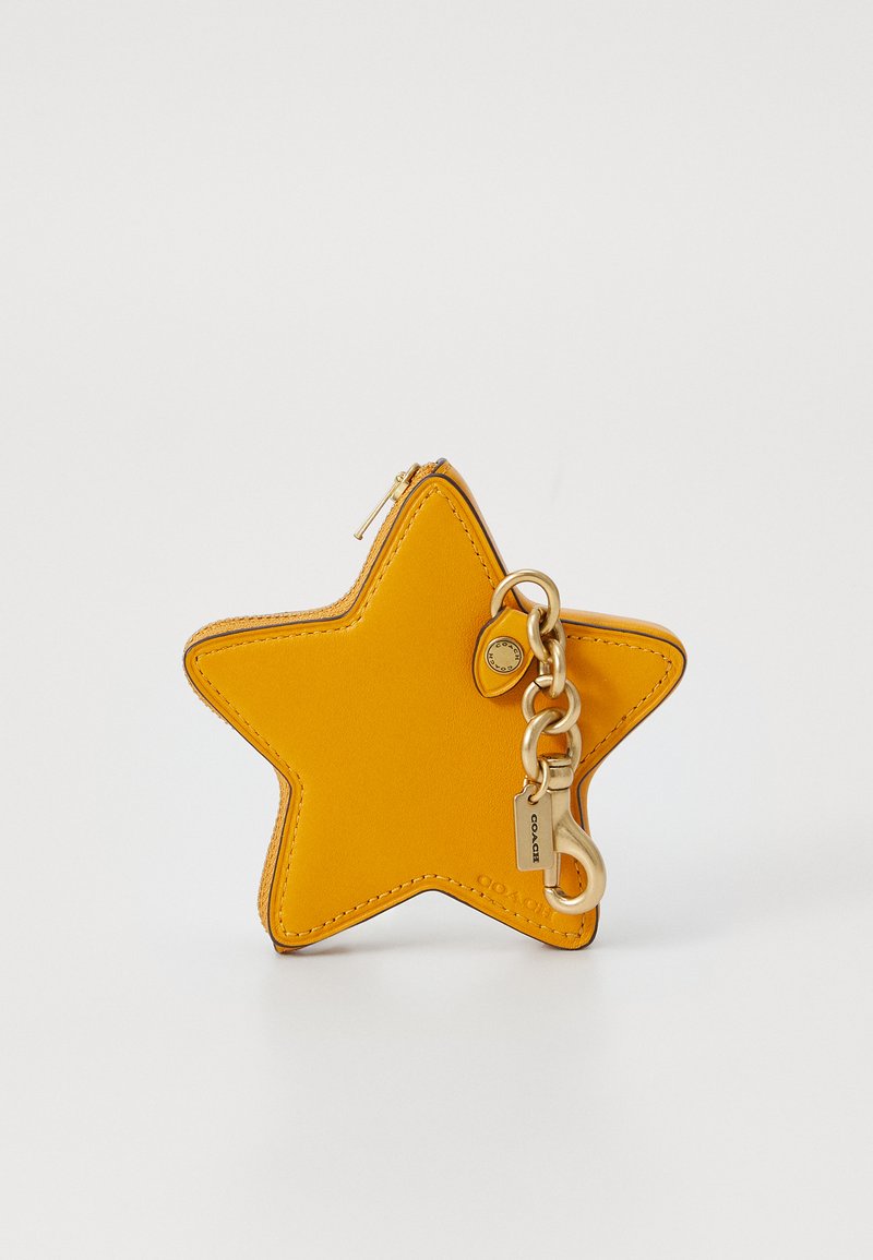 Dzeltena ādas zvaigznes formas atslēgu piekariņu maiss ar zelta rāvējslēdzēju un aparatūru. Iezīmē izšūtas malas un dekoratīvu sprādzi.