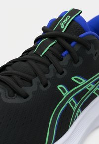 Μαύρο αθλητικό παπούτσι με πράσινες και μπλε λεπτομέρειες, διαθέτοντας υφή στην επάνω επιφάνεια, ραμμένες λεπτομέρειες και παραδοσιακό σύστημα κορδονιών.