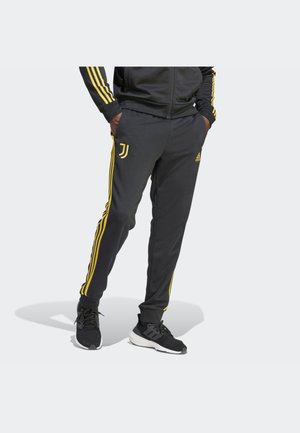 Pantalones deportivos negros con rayas amarillas de Adidas, ajuste tapered, cintura elástica y bolsillos laterales. Presenta el logo de la Juventus en el muslo izquierdo.