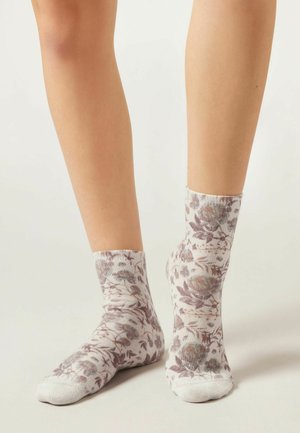 Blommiga ankelsockor i ljusa pastellfärger. Har ett texturerat mönster med löv och blommor i nyanser av lila och grått. Mjuk material.