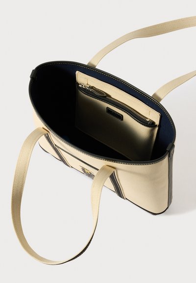 Saco de lona bege com detalhes em couro preto, bolso interior com fecho éclair e forro em tecido. Alças duplas em tecido para transporte.