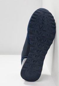Semelle de baskets bleu marine avec motifs géométriques de la bande de roulement et logo "Skechers" en relief sur la semelle en caoutchouc.
