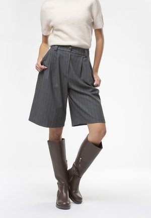Pantaloni corti a vita alta grigi con righe, dotati di tasche laterali, abbinati a stivali alti in pelle marrone con cerniere laterali. Maglia in maglia beige morbida.