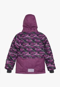 Giacca con cappuccio a motivo camouflage viola e nero, tessuto testurizzato e polsini regolabili. Presenta una toppa bianca sul retro.
