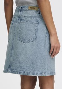 Light blue denim skirt with a straight cut, two back pockets, and a label marked "ICHI" on the waistband. Textured, mid-length design.
