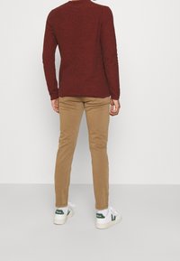 Donkerrode gebreide longsleeve shirt, gecombineerd met beige broek en witte sneakers met groene accenten. De textuur lijkt zacht en casual te zijn.