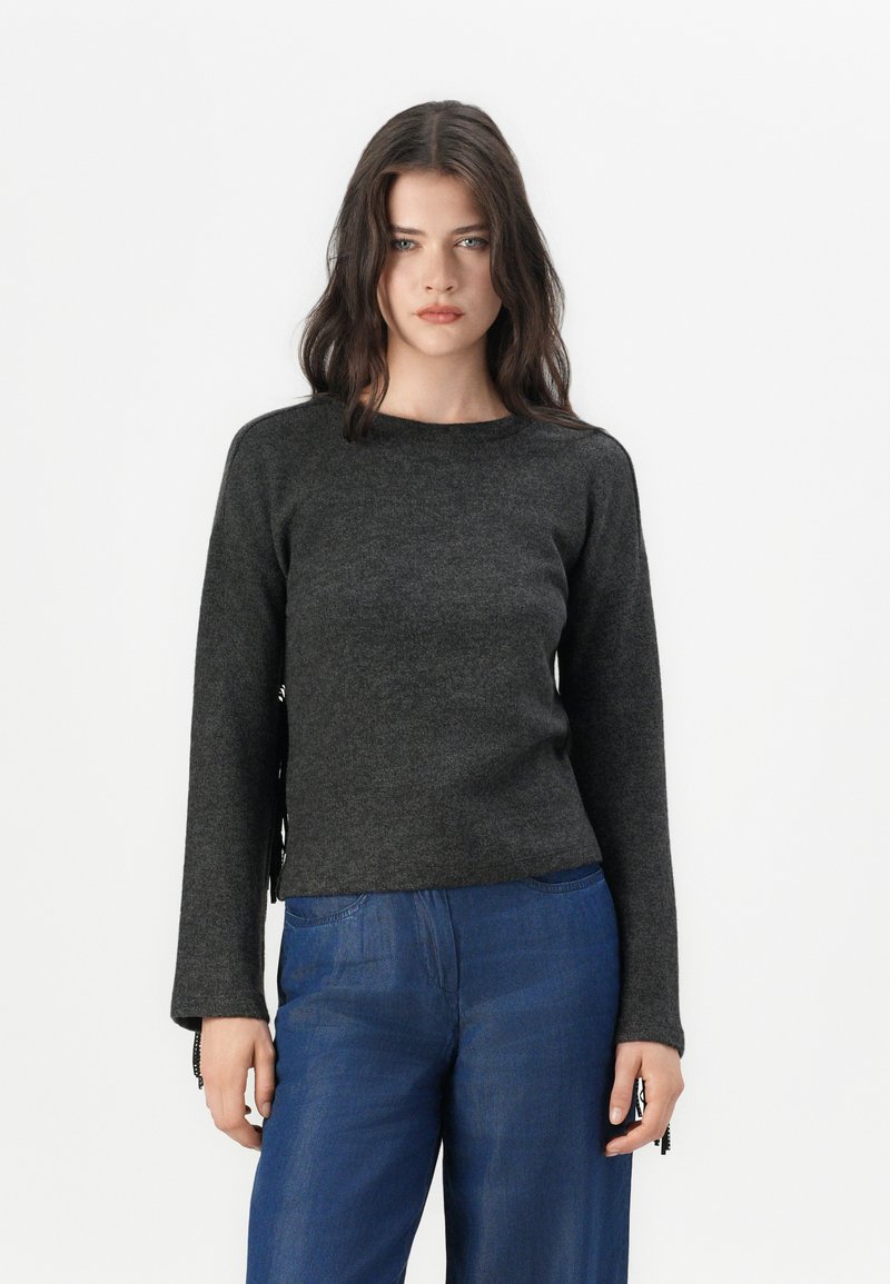 Dunkelgrauer Langarmpullover mit Rundhalsausschnitt, weicher Textur, mit seitlichen Schlitzungen und schwarzen dekorativen Akzenten an den Bündchen. Kombiniert mit blauen Hosen.