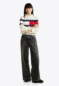 Hvid cropped sweater med røde, marineblå og blå striber, med "TOMMY JEANS"-logo; stylet med sorte bukser med vide ben og sorte sko.