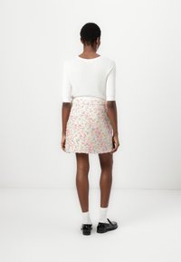 Haut blanc à manches courtes associé à une mini-jupe en tweed pastel avec des éclats multicolores. Des chaussures noires et des chaussettes blanches complètent le look.