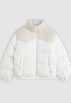 Doudoune avec un col haut, présentant une section supérieure crème et un corps blanc, texture matelassée, poches avant et poignets élastiques.