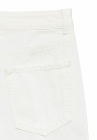 Détail de la poche arrière d'un jean en denim blanc montrant les coutures, la passants de ceinture et la texture du tissu sur un fond uni.