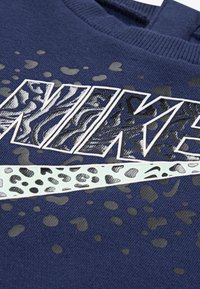 Granatowy sweatshirt z dużą grafiką "NIKE" w czerni i srebrze, z akcentem w leopardzi wzór na logo oraz teksturowanym materiałem.