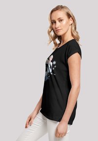 T-shirt noir en coton avec un design graphique d'un personnage avec des flocons de neige. Manches courtes et coupe décontractée, associé à un pantalon blanc.