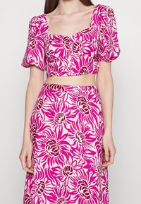 Vaaleanpunainen kukkakoristeinen lyhythihainen paita, jossa on puffihihat, neliönmuotoinen kaula-aukko ja nappitodistus; vastaava lentävä hame, jossa on samankaltainen kirkas kukkakuosi.