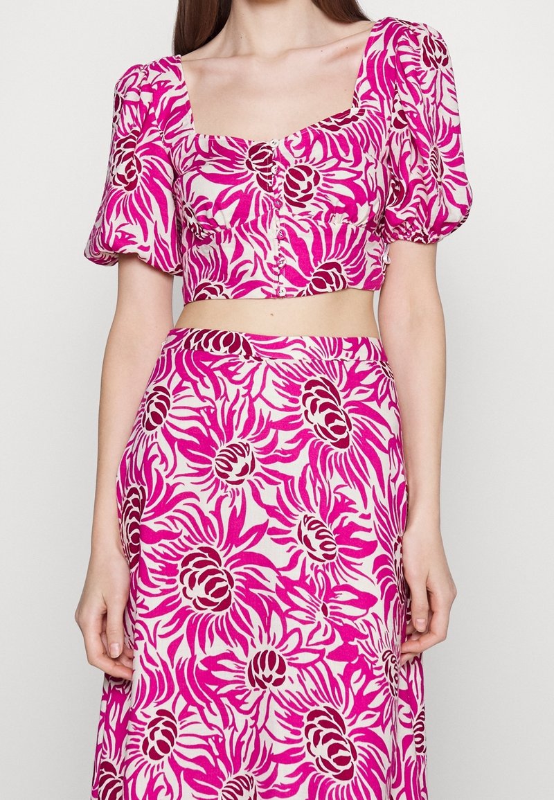 Vaaleanpunainen kukkakoristeinen lyhythihainen paita, jossa on puffihihat, neliönmuotoinen kaula-aukko ja nappitodistus; vastaava lentävä hame, jossa on samankaltainen kirkas kukkakuosi.