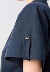 Granatowa koszula z krótkim rękawem o strukturalnym kołnierzyku i wykończeniu, z detalem mankietu zapinanego na guziki oraz gładką, lekką fakturą materiału.