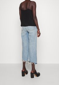 Svart ärmlös topp med tunna axelband, tillsammans med ljusblå vida jeans med fransar i nederkant, och svarta platåskor.