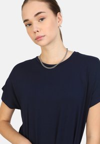 T-shirt corta a maniche corte di colore blu navy, realizzato in tessuto liscio con una vestibilità comoda. Indossato con una collana in argento, caratterizzata da un design a strati.