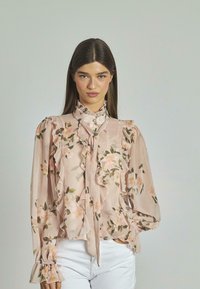Blusa floreale in chiffon rosa chiaro, con dettagli arricciati, maniche lunghe e colletto alto con un fiocco. Motivo di fiori e foglie.