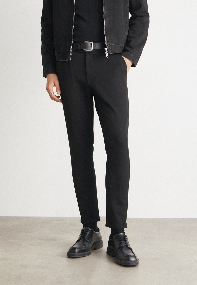 Black pants with a tailored fit, paired with a zippered black jacket. Black leather shoes and a black belt complete the look. Smooth texture.