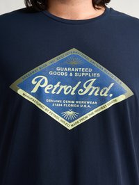 Námořnická modrá tričko s velkým, diamantovým grafickým potiskem ve zlaté a modré barvě, uvádějící "Petrol Ind." se stylem vintage a slunečními paprsky.