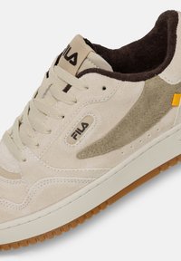 Vit mockaskor med bruna accenter, med en strukturerad logopatch, beige snören och en sula i gummirubber. Rund tå och sydda detaljer.