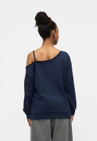 Μπλε σκούρο φούτερ χωρίς ώμους με μακριά μανίκια και άνετη εφαρμογή, με εκτεθειμένο τμήμα ώμου και ριμπ μανσέτες. Ύφασμα από βαμβακερό μείγμα.