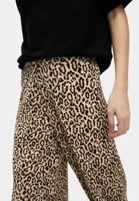 Sukně s potiskem leopardí kůže v béžové a černé barvě, vyrobené z texturované tkaniny a volného střihu. Nosené s černým oversized topem.
