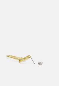 Boucle d'oreille en métal doré avec un design tordu et une pièce de fond argentée, dotée d'un tige droite pour la fixations dans l'oreille.