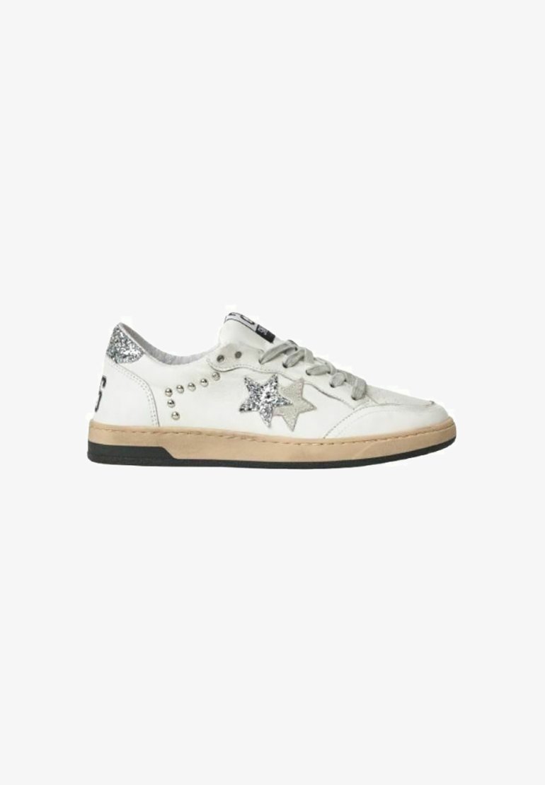 Witte leren sneaker met beige zool, grijze veters, zilveren glitterster en studs, en een zilveren glitterdetail op de hiel, op een witte achtergrond.