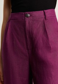 Fuchsia linnen hoge taillebroeken met een nauwsluitende pasvorm, voorzien van een glazen knoopsluiting en subtiele voorplooien voor extra structuur.