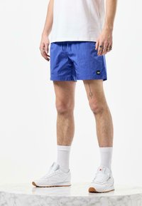 Lyseblå shorts lavet af let materiale med elastisk talje, parret med hvide sneakers og ribbet hvide sokker. Bemærkelsesværdig logo detalje.