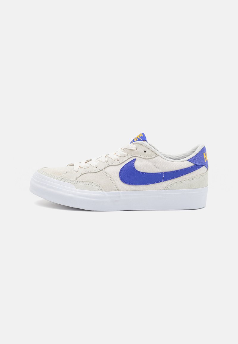 Sneaker bej din suede, cu un swoosh din piele albastră, talpă din cauciuc alb și branding galben pe limbă. Închidere cu şireturi, cu guler căptușit.