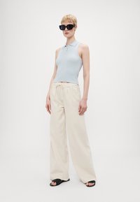 Top polo senza maniche a coste blu chiaro abbinato a pantaloni ampi color crema, con coulisse. Occhiali da sole oversize neri completano il look.