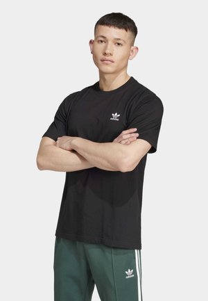 Zwarte katoenen t-shirt met korte mouwen, voorzien van een witte Adidas-logo op de linkerkant van de borst. Draagt een groene trainingsbroek.