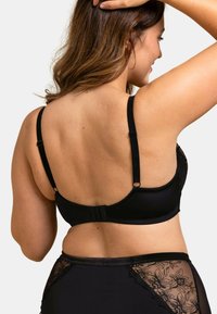 Soutien-gorge noir avec bretelles réglables, texture lisse et fermeture à crochet sécurisée. Accents en dentelle florale notables sur les côtés.