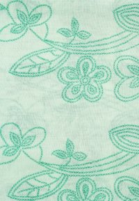 Lichtgroene stof met geborduurde bloem- en bladvormen in een donkerdere groene draad, met gebogen lijnen en verfijnde details.