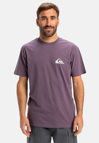 Purple cotton t-shirt featuring a crew neck, short sleeves, and a white logo on the left chest. Smooth texture, casual fit.