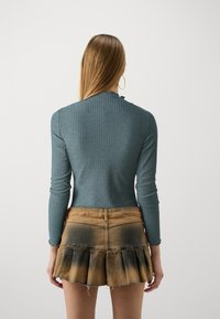 Haut à manches longues côtelé couleur sarcelle associé à une jupe courte en denim à volants, présentant un dégradé du brun clair au brun foncé.