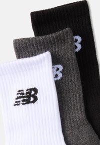 Conjunto de tres calcetines en blanco, gris y negro, con textura acanalada y un pequeño logotipo "NB" en colores contrastantes en cada calcetín.