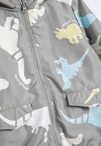 Waterbestendige grijze jas met kleurrijke dinosaurussenprints in blauw, geel en wit, voorzien van een rits en details van een vo zak.