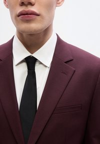 Μπουφάν κουστουμιού μπ ορντό με αποσπώμενο πέτο, εφαρμοστή γραμμή, μία τσέπη στο στήθος, συνδυασμένο με λευκό πουκάμισο και μαύρη γραβάτα. Λείο υφασμάτινο ύφασμα.