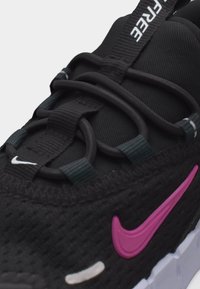 Κοντινό πλάνο μαύρου αθλητικού παπουτσιού Nike με μοβ σήμα, μαύρα κορδόνια που περνούν μέσα από υφασμάτινους κρίκους και λαβή με λευκό κείμενο στη γλώσσα.