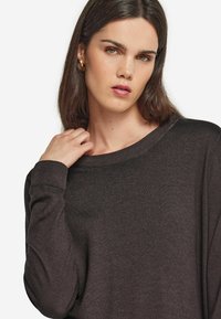 Mörkbrun tröja med löst sittande passform, bred halsringning och ribbade manschetter. Mjuk textur och minimalistisk design. Accentuerad av eleganta, gyllene hoops. 