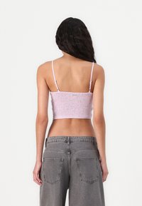 Smokket lilla crop top med tynne justerbare stropper, sammen med høyt liv, falmede grå denimjeans med baklommer.