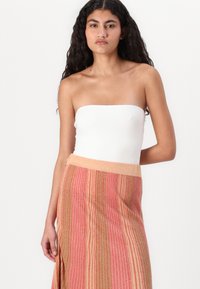 Haut blanc sans bretelles associé à une jupe maxi rayée multicolore présentant des teintes de rose, d'orange et de vert, avec une finition texturée.